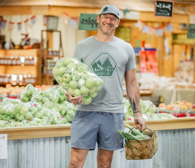 a man holding a bag of fresh apples and corn